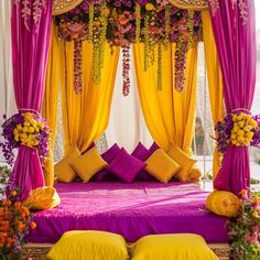 a bed covered in yellow and purple drapes with lots of flowers on the headboard