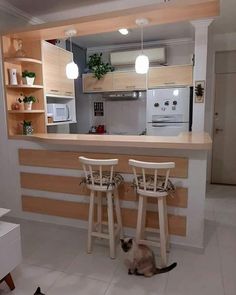 two cats sitting on the floor in front of a kitchen counter with stools next to it