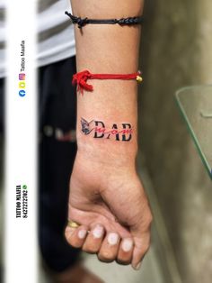 a person with a tattoo on their wrist holding the hand of another person wearing a red string bracelet