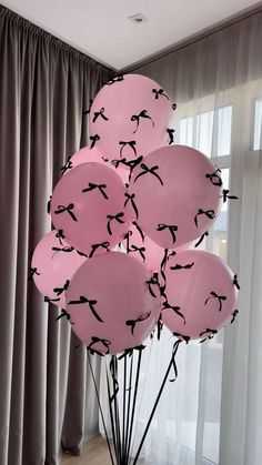 a bunch of pink balloons with black birds on them in front of a curtained window