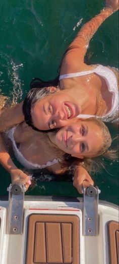 two women in white bathing suits on a boat with their arms around each other and smiling at the camera