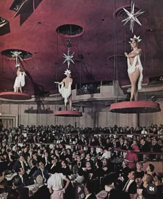 an old photo of some people on stage in front of a large audience with stars hanging from the ceiling