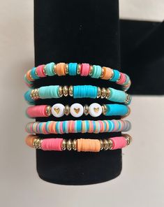 multicolored bracelets with buttons and gold accents on a black display stand in front of a white background