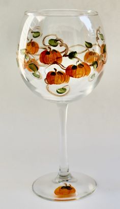 a wine glass with pumpkins painted on the side and leaves in the middle, sitting against a white background