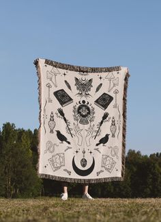 a person standing in the grass with a blanket over their head that has various symbols on it