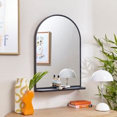 a mirror sitting on top of a wooden table next to a lamp and potted plant