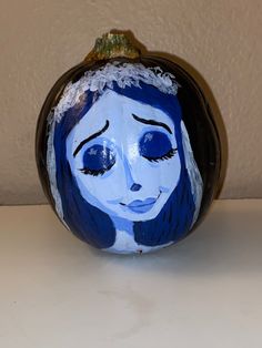 a blue painted pumpkin with a woman's face on the front and side, sitting on a table