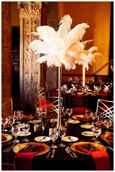 a tall centerpiece with white feathers sits on top of a table set for an event