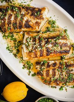 grilled fish on a white platter with lemons and parmesan cheese