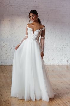 a woman in a white wedding dress standing on a wooden floor with her arms behind her back