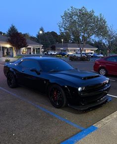 a black sports car parked in a parking lot next to other cars and buildings at dusk