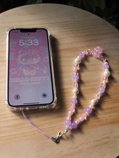 a cell phone with a pink beaded lanyard next to it on a wooden table