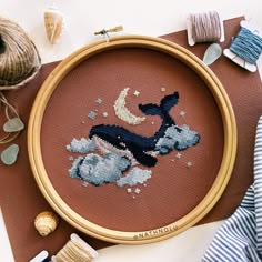 a cross - stitch whale with the moon and clouds on it's back in a wooden frame