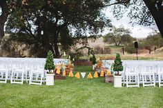 an outdoor ceremony setup with white chairs and yellow decorations on the grass in front of trees