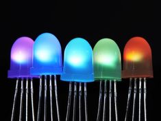 four different colored lights sitting next to each other on top of metal pins in front of a black background