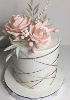 there is a white cake with pink flowers on top and gold wire around the edges