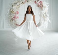 a woman in a white dress is standing under a floral arch