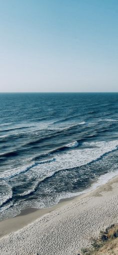 an ocean view from the top of a hill with waves coming in to shore and blue sky above