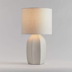 a white table lamp with a beige shade on the base and a light bulb attached to it