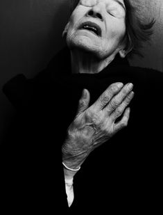 an older woman with her eyes closed and hands folded in front of her face, leaning against a wall