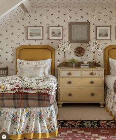 two beds in a room with floral wallpaper and pictures on the walls above them