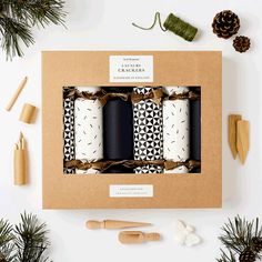 three candles in a cardboard box surrounded by pine cones and other holiday decorations on a white surface