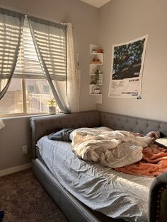 an unmade bed in a bedroom next to a window