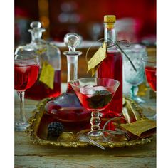 some wine glasses and bottles are on a tray with gold trimmings, one is filled with red liquid the other has blackberries in it