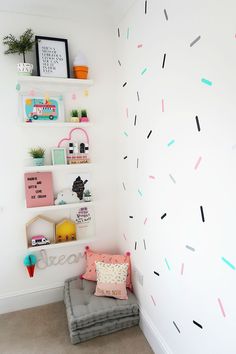 a white wall with colorful sprinkles on it and a gray cushion in the corner