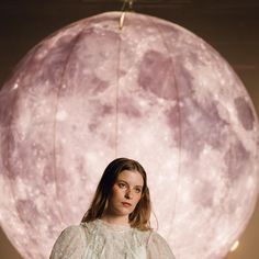 a woman standing in front of a giant pink moon light hanging from a ceiling fixture