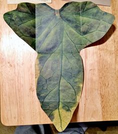 a piece of art made out of leaves on top of a cutting board with scissors