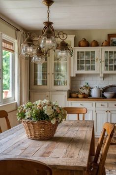 a wooden table sitting under a chandelier next to a kitchen counter with flowers in a basket on it