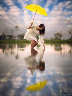 a woman in white dress holding an umbrella over her head and standing on the edge of a body of water