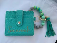 a turquoise wallet with a tassel and keychain attached to it, sitting on top of a white sheet