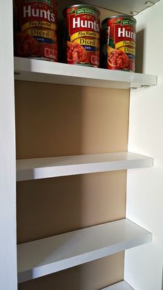 two cans of humps on top of shelves in a kitchen cabinet with white shelving