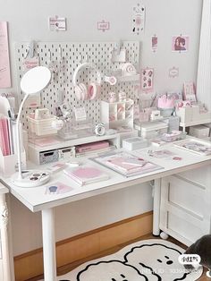 a white desk topped with lots of pink and white items next to a wall covered in pictures