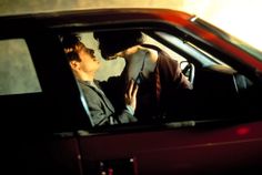 a man and woman kissing in the back seat of a red car with their hands on each other's hips