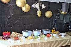 a table topped with lots of food next to hanging lights and paper lantern shades on the wall