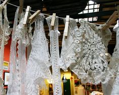 many white laces are hanging on a clothes line in an antique store, some with holes and crochets