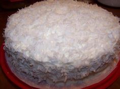 a close up of a cake with white frosting on a red plate and a potted plant in the background