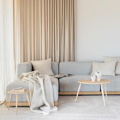 a living room with a gray couch and two tables in front of a curtained window