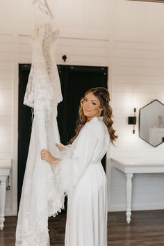 a woman standing next to a wedding dress hanging on a rack in a room with white walls