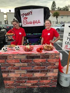 two women in red shirts are standing behind a brick table with food on it and a sign that says spook chickee