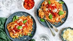 two plates of spaghetti with sauce, cheese and spinach on the side next to glasses of water