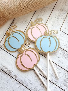 three pink and blue cake pops on a white wooden table next to burlock