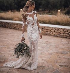 a woman in a wedding dress holding a bouquet and wearing a long sleeved gown