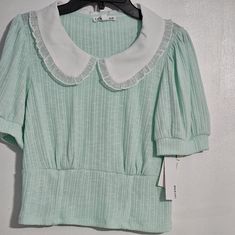 Elevate Your Girl's Wardrobe With This Stunning Lily Star Tee In Size M. The Mint And White Color Combination Is Perfect For Any Outdoor Festival Or Casual Event. The Shirt Features A Stylish Baby Collar And Short Sleeves, Making It A Comfortable And Fashionable Choice For Your Little One. The Solid Pattern And Basic Style Of This Top Make It A Versatile Addition To Any Girl's Wardrobe. Whether Your Daughter Is Dressing Up For A Special Occasion Or Simply Hanging Out With Friends, This Shirt Is Trendy Cotton Tops With Cute Collar, Cute White Top With Peter Pan Collar, Casual White Tops With Cute Collar, Casual Summer Top With Cute Collar, Casual White Top With Peter Pan Collar, Cute Spring Tops With Collar, Cute Peter Pan Collar Top For Spring, Cute Cotton Tops With Peter Pan Collar, Casual Cotton Top With Peter Pan Collar