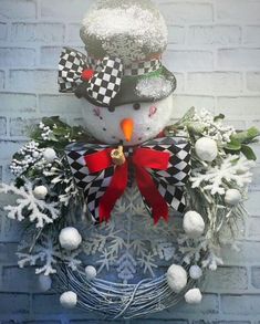 a snowman is sitting on top of a wreath with red bow and black and white decorations