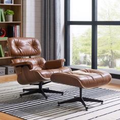 an eames chair and ottoman in front of a large window with bookshelves