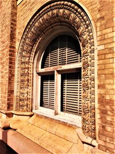 an ornate window with shutters on the side of a brick building